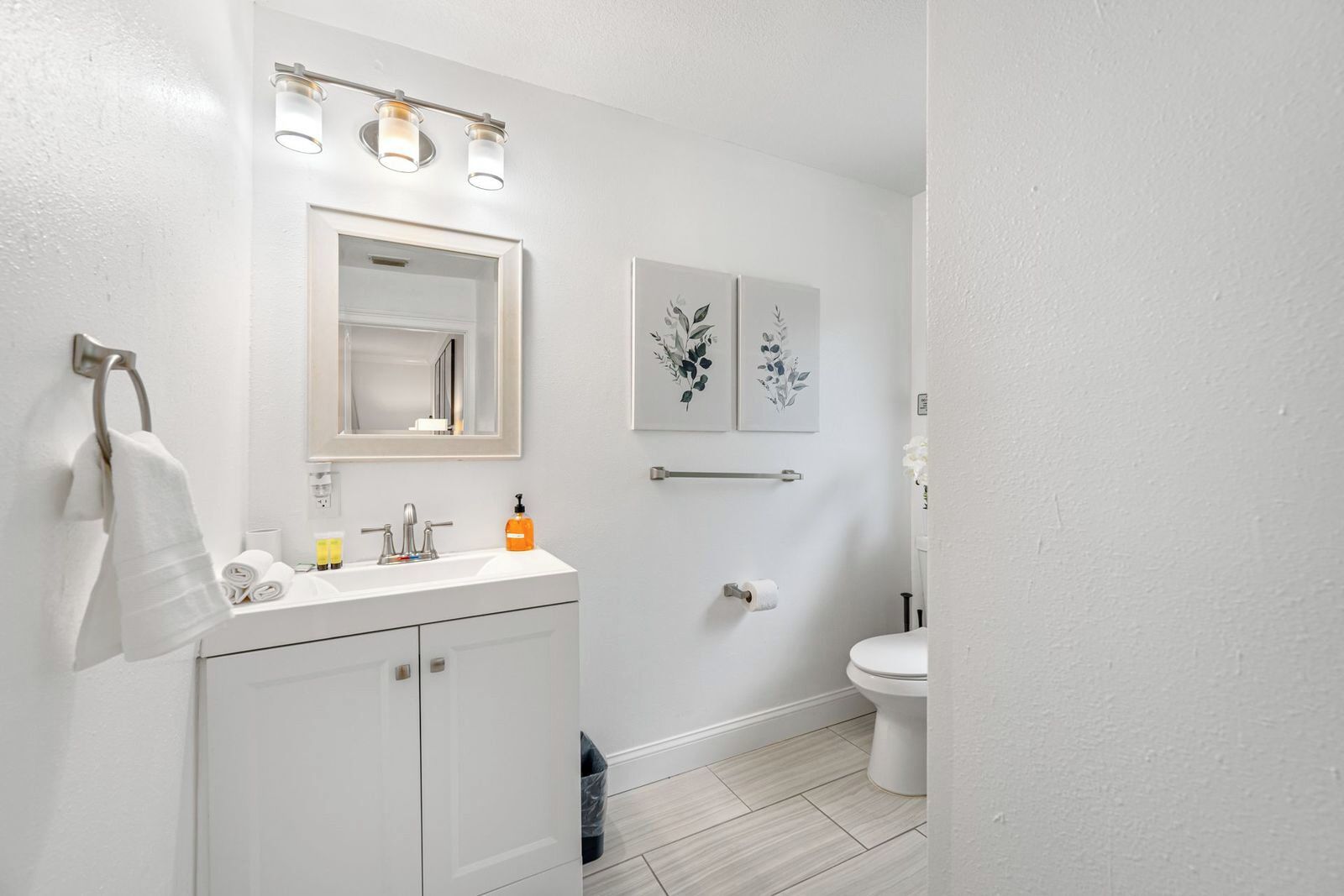 Une salle de bain avec un meuble-lavabo blanc, un miroir, un porte-serviettes, des toilettes et deux appliques murales.