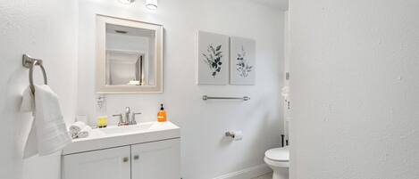 Une salle de bain avec un meuble-lavabo blanc, un miroir, un porte-serviettes, des toilettes et deux appliques murales.