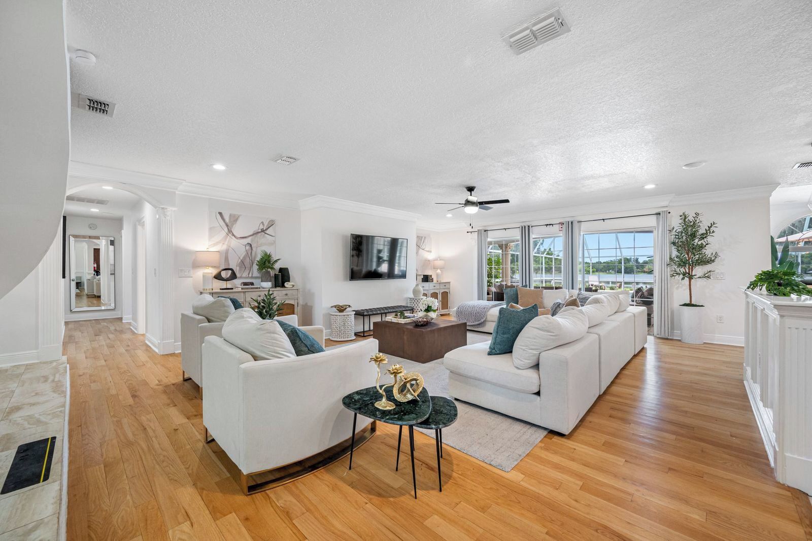 A spacious living room with a white sofa set, a coffee table, and a television mounted on the wall.