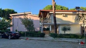 A residential building with a paved driveway, a parked car, and a tree in the foreground.