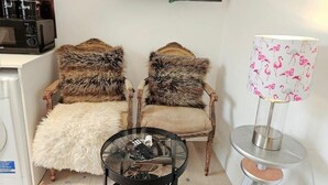 A living room with two fur-covered chairs, a glass coffee table with a remote control, a television mounted on the wall, and a lamp with a flamingo pattern. - Central London Studio for 2 with Kitchenette (London)