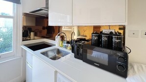 A compact kitchen with white cabinets, a built-in microwave, a toaster, and a coffee maker. - Central London Studio for 2 with Kitchenette (London)