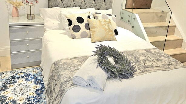 A bedroom with a bed, a nightstand, a mirror, a staircase, and a wall-mounted thermostat. - Central London Studio for 2 with Kitchenette (London)