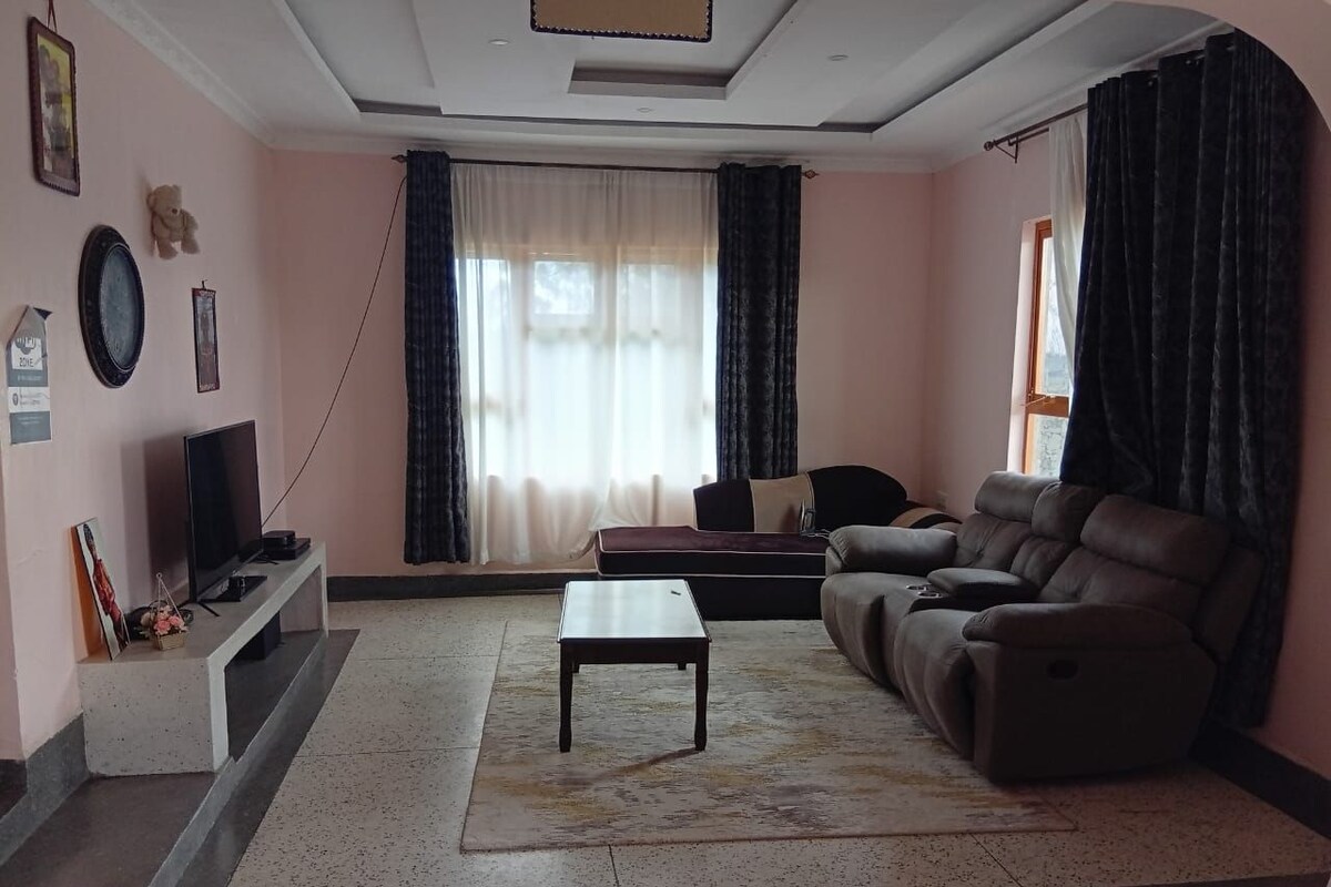 A living room with a sofa, a TV, a coffee table, and a window with curtains.