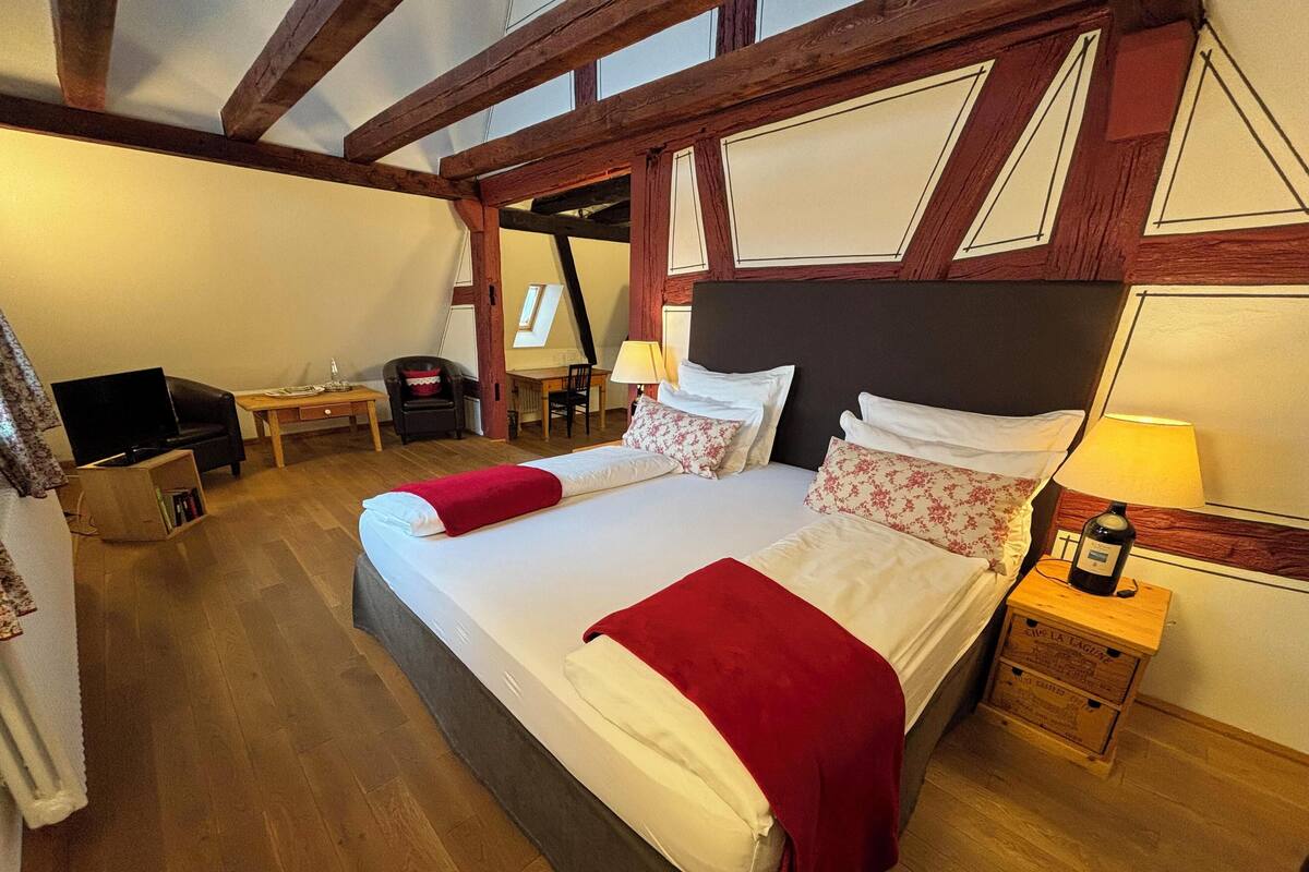 A hotel room with a large bed, two bedside tables with lamps, a desk, a chair, and a television.