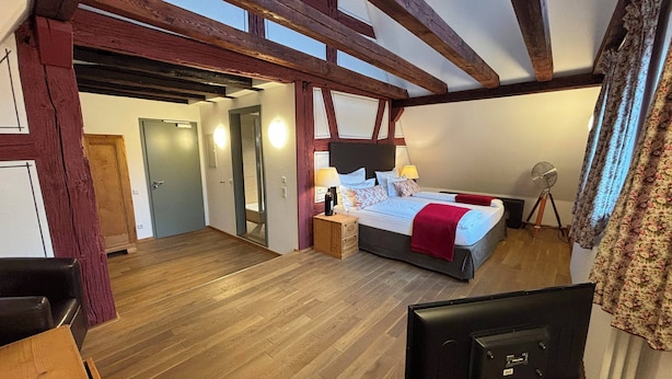 Un dormitorio con una cama grande, vigas de madera, un televisor y un ventilador.