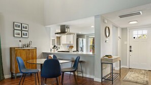 A modern kitchen with white cabinets, a stainless steel range hood, and a dining area with a round table and blue chairs. - Alexandria Dr xxxxxx (Austin)