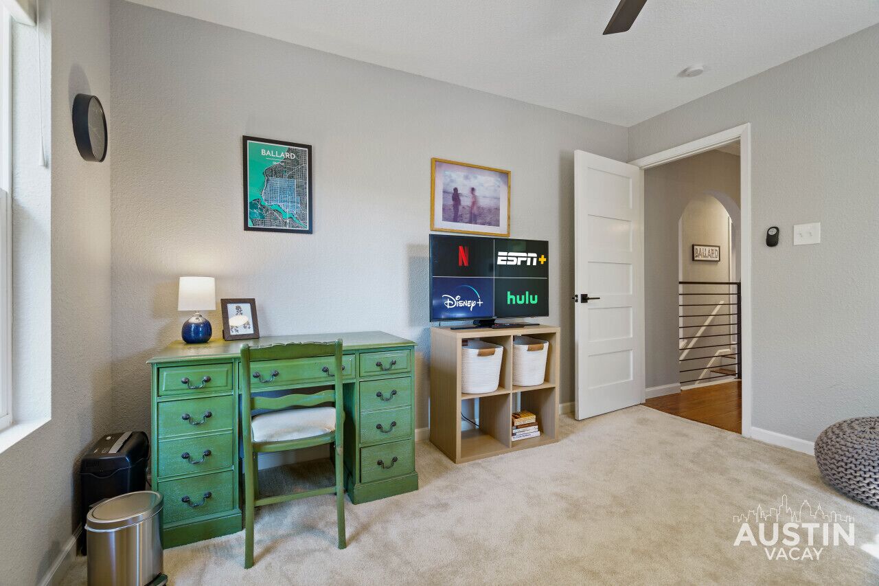 Quarto com escrivaninha, cadeira, lixeira, estante com cestos de arrumação e porta que dá para outro espaço.
