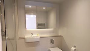 Un bagno moderno con cabina doccia in vetro, un lavabo bianco con specchio sopra e un water.