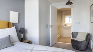Una camera da letto moderna con un letto, un comodino, una lampada e una poltrona grigia.