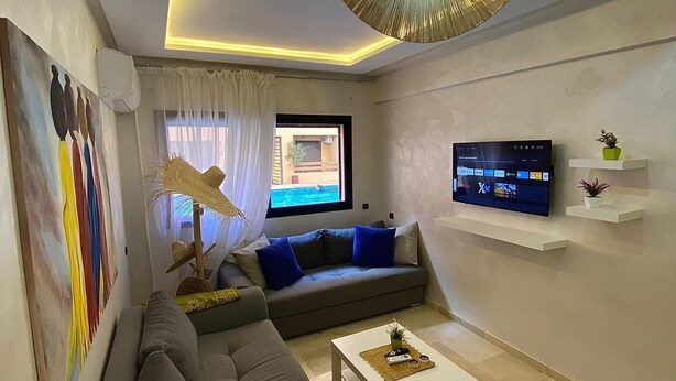 Una sala moderna con un sofá seccional gris, una mesa de centro blanca, un televisor de pantalla plana montado en la pared y una lámpara de techo.