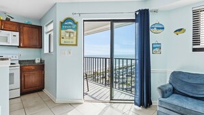 A kitchen with wooden cabinets, a microwave, and a view of the beach through a sliding glass door. - T1012 at Myrtle Beach Resort (Myrtle Beach)