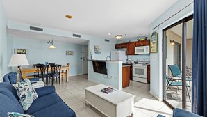 A modern living room with a sofa, coffee table, and a TV. There is a kitchen area with a microwave, stove, and dining table. - T1012 at Myrtle Beach Resort (Myrtle Beach)