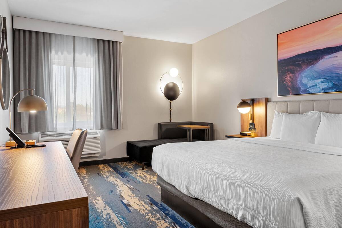 Hotelkamer met een groot bed, een bureau, een stoel, een lamp, een nachtkastje en een schilderij aan de muur.