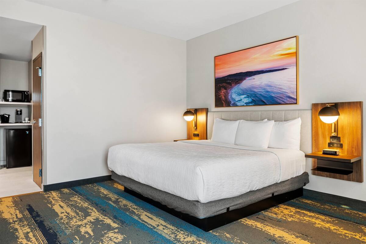 Hotelkamer met een bed, een zonsondergangschilderij, een magnetron en een koffieapparaat.