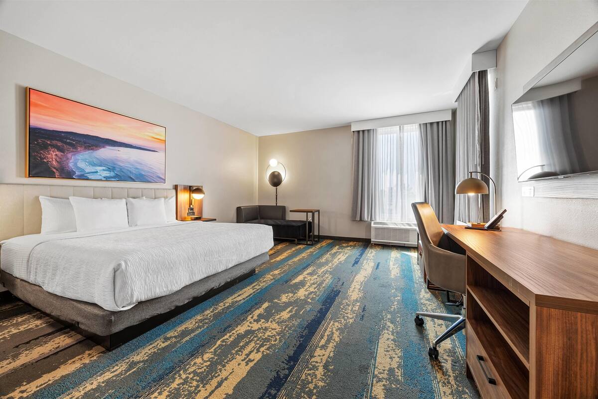 Een hotelkamer met een groot bed, een bureau, een stoel, een televisie en een schilderij aan de muur.