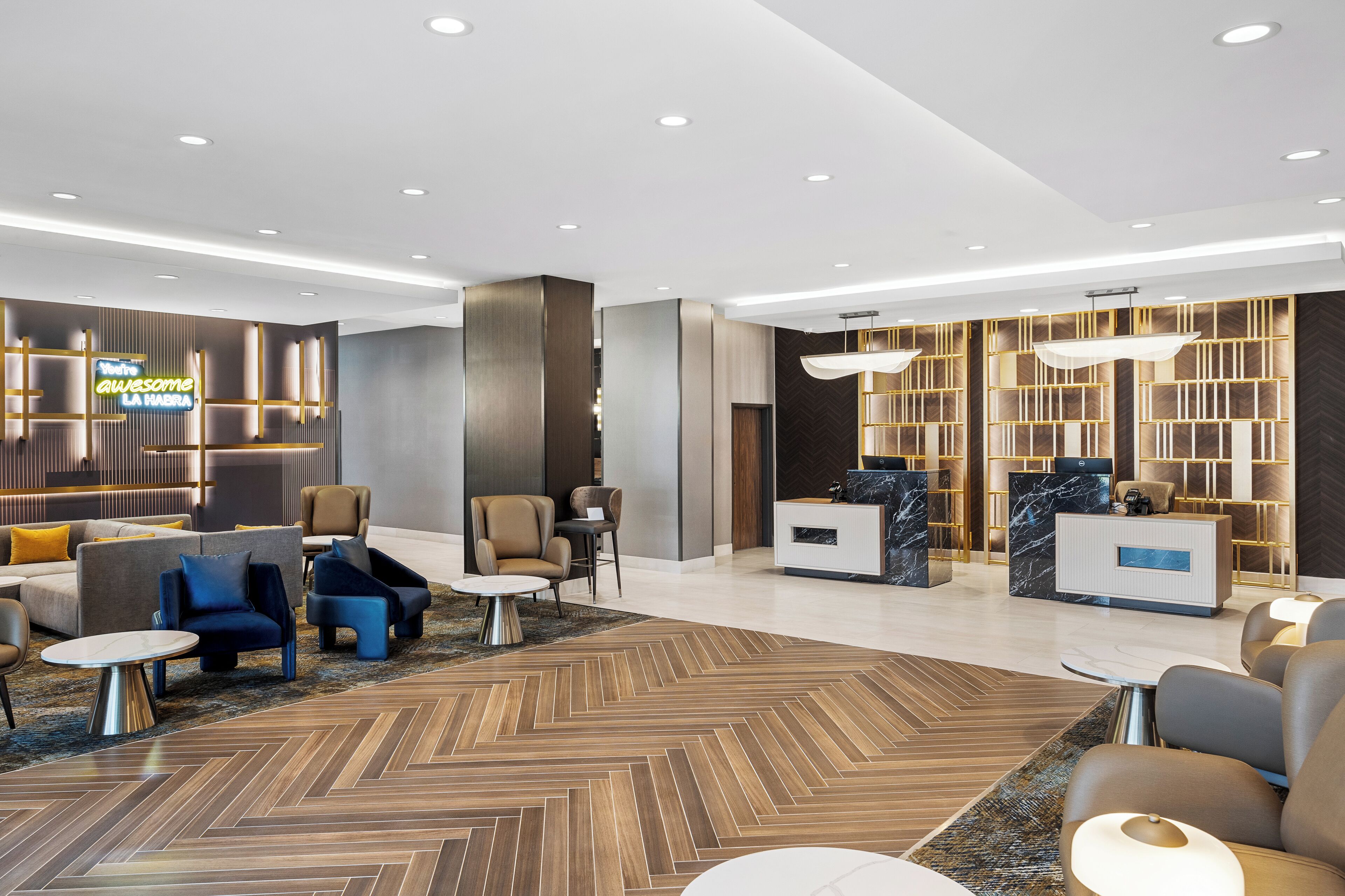 A modern hotel lobby with a reception desk, seating areas, and a herringbone-patterned floor.