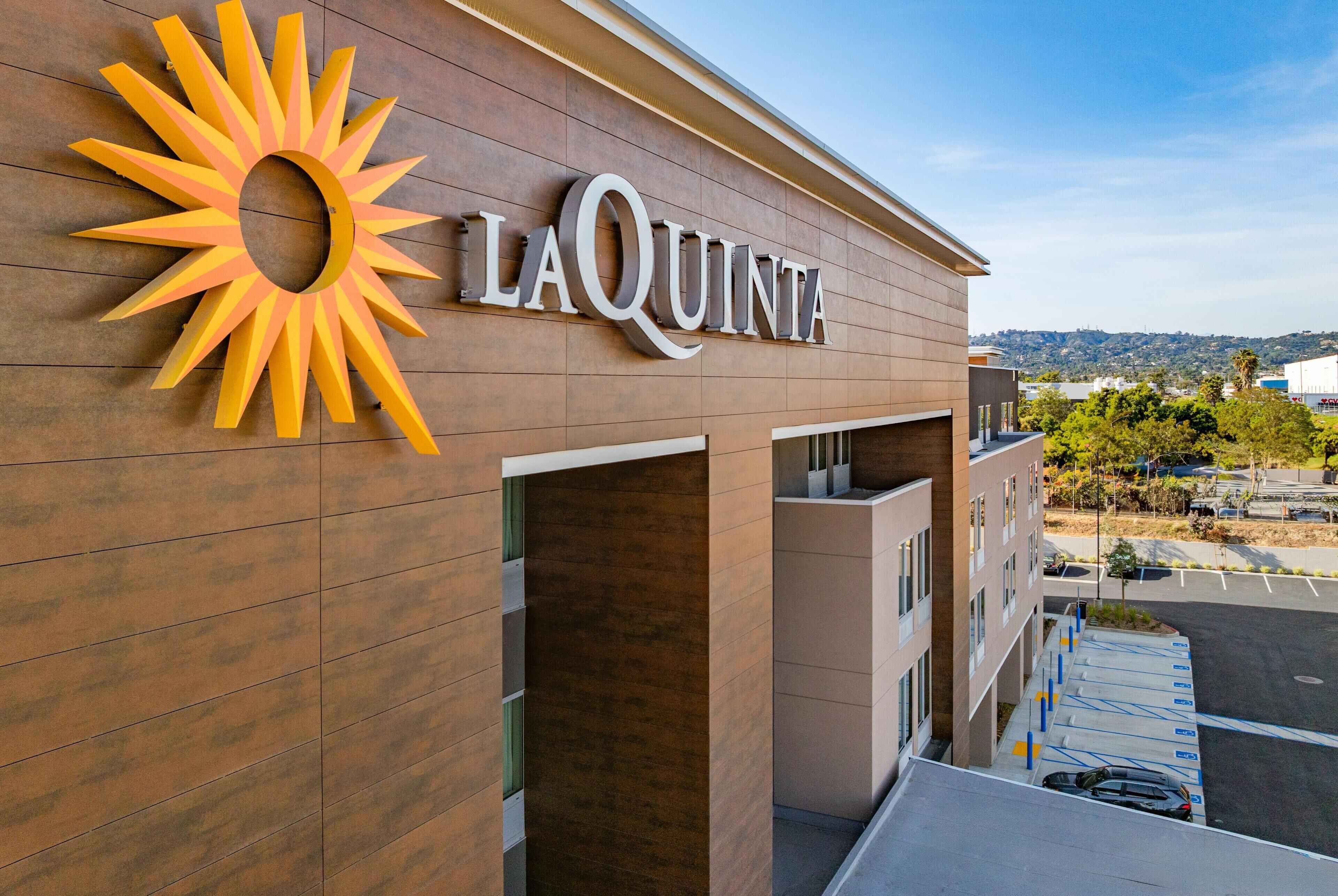 A hotel with a sun-shaped logo, a modern facade, and a parking lot.