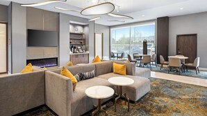 A modern hotel lobby with a sectional sofa, a fireplace, a flat-screen TV, and a dining area with tables and chairs. - La Quinta Inn & Suites by Wyndham La Habra (La Habra)