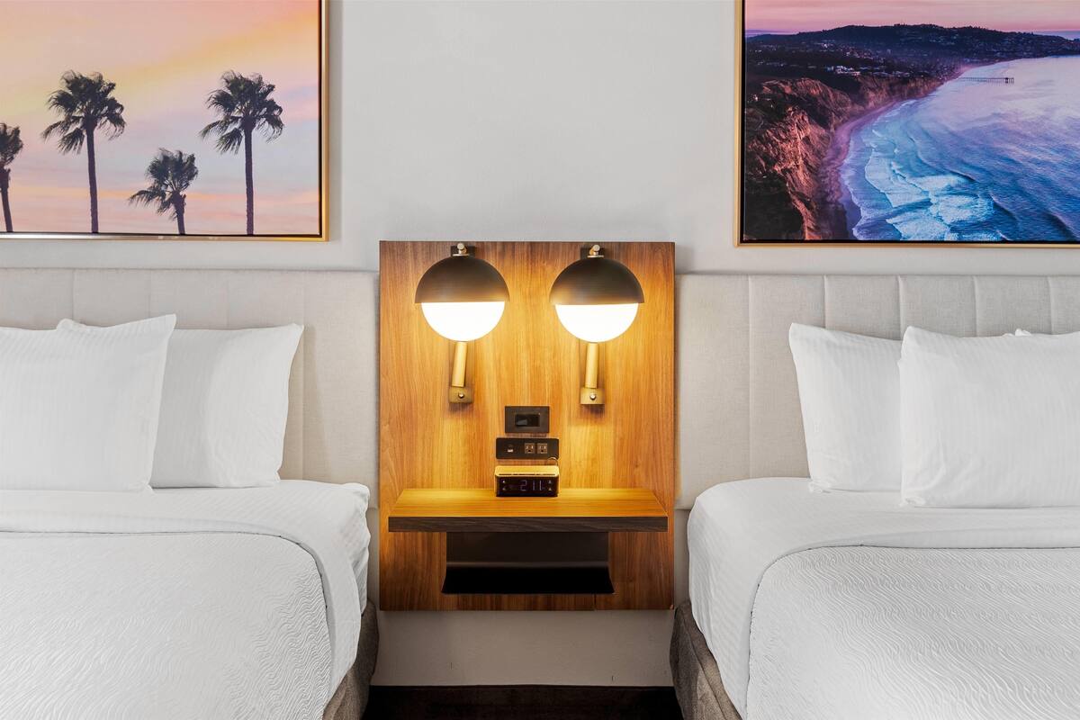 Een hotelkamer met twee bedden, een houten hoofdbord, een nachtkastje met een klok en twee wandlampen.