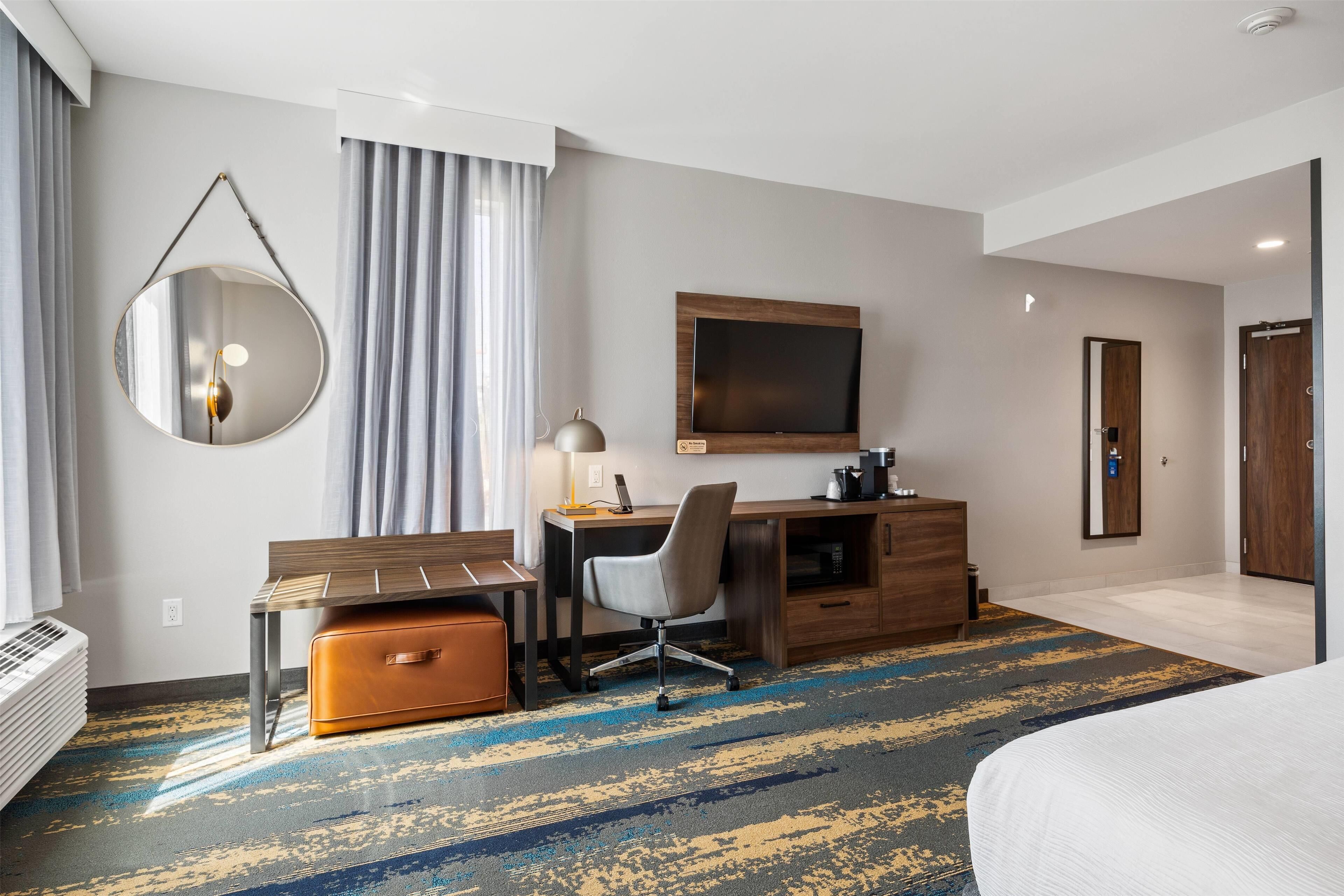 Habitación de hotel con cama, escritorio, silla y un espejo grande.