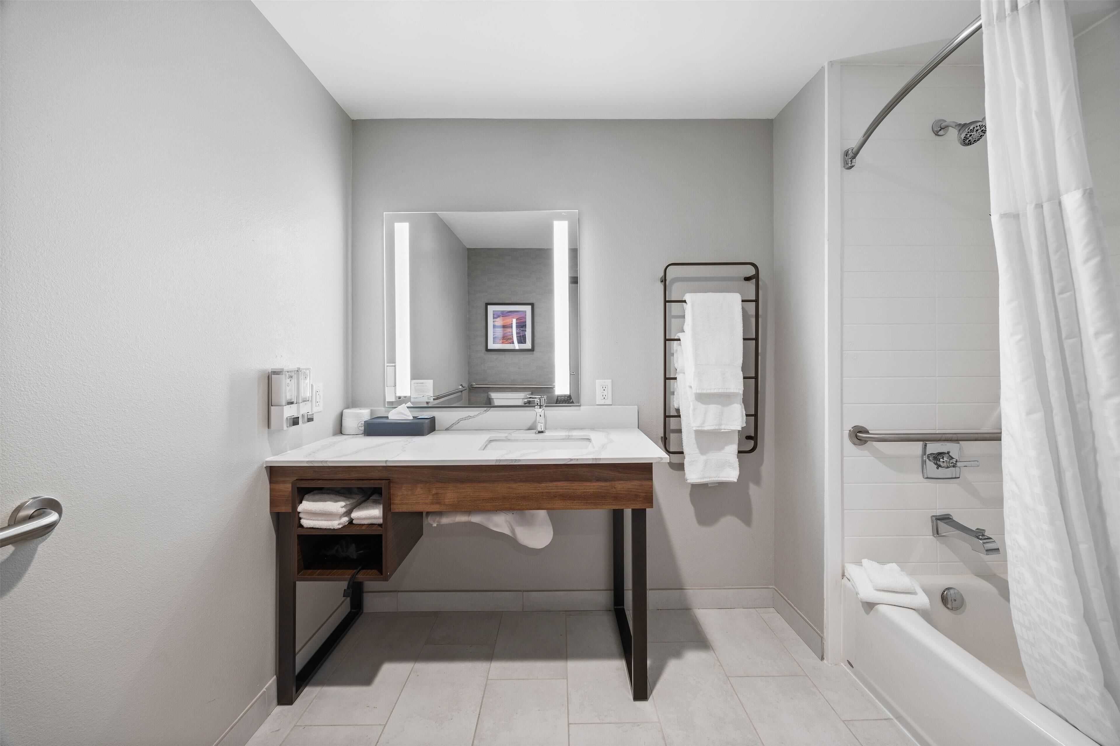 A modern bathroom with a wooden vanity, a large mirror, a shower with a glass door, and a towel rack.