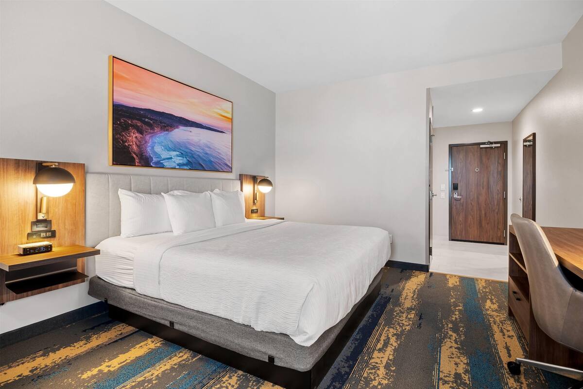 Een hotelkamer met een groot bed, nachtlampjes, een bureau en uitzicht op de oceaan.
