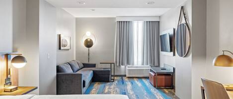 Ein modernes Hotelzimmer mit einem großen Bett, einer Couch, einem kleinen Tisch und einem Schreibtisch.