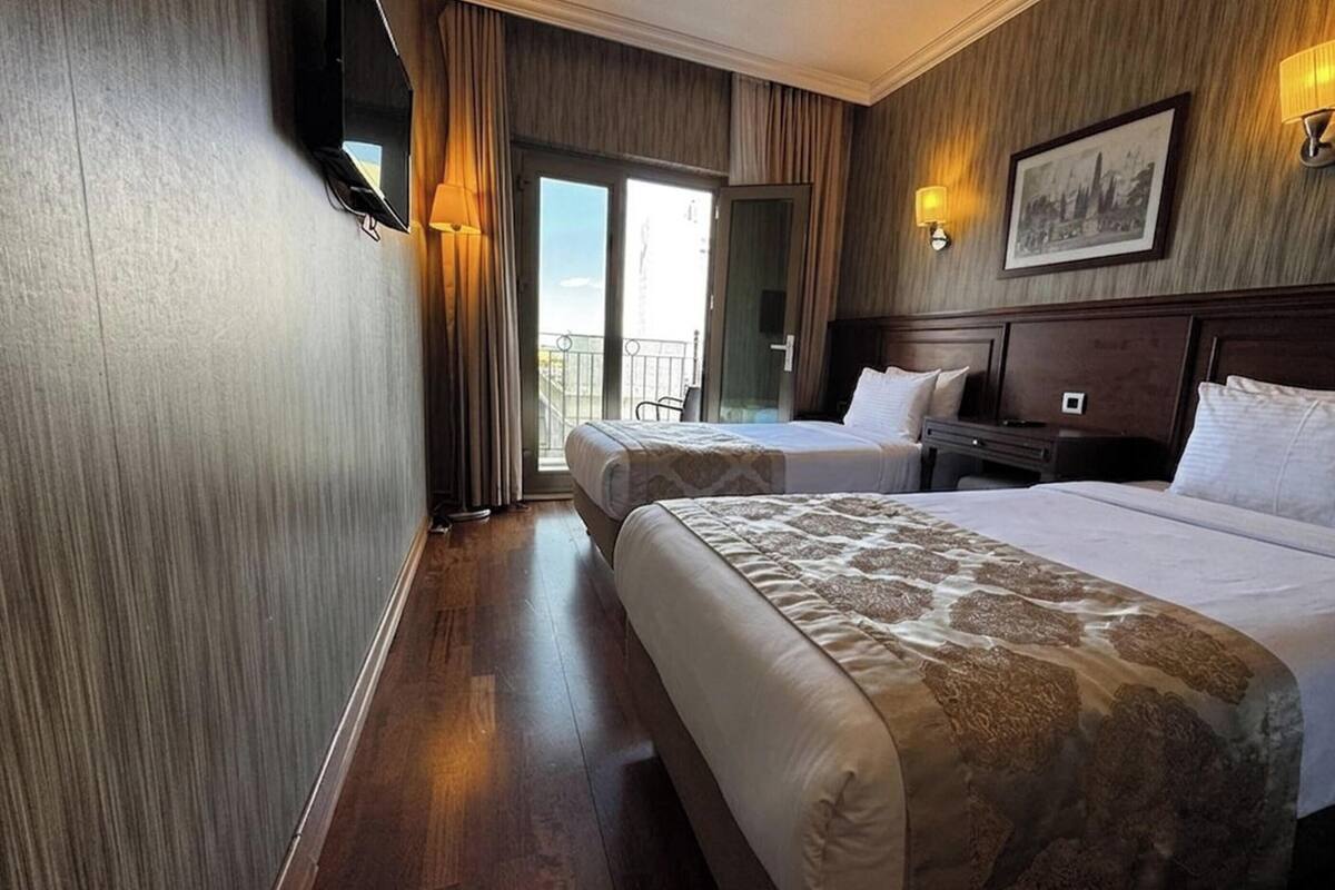 A hotel room with two beds, a flat-screen TV, a painting on the wall, and a balcony.