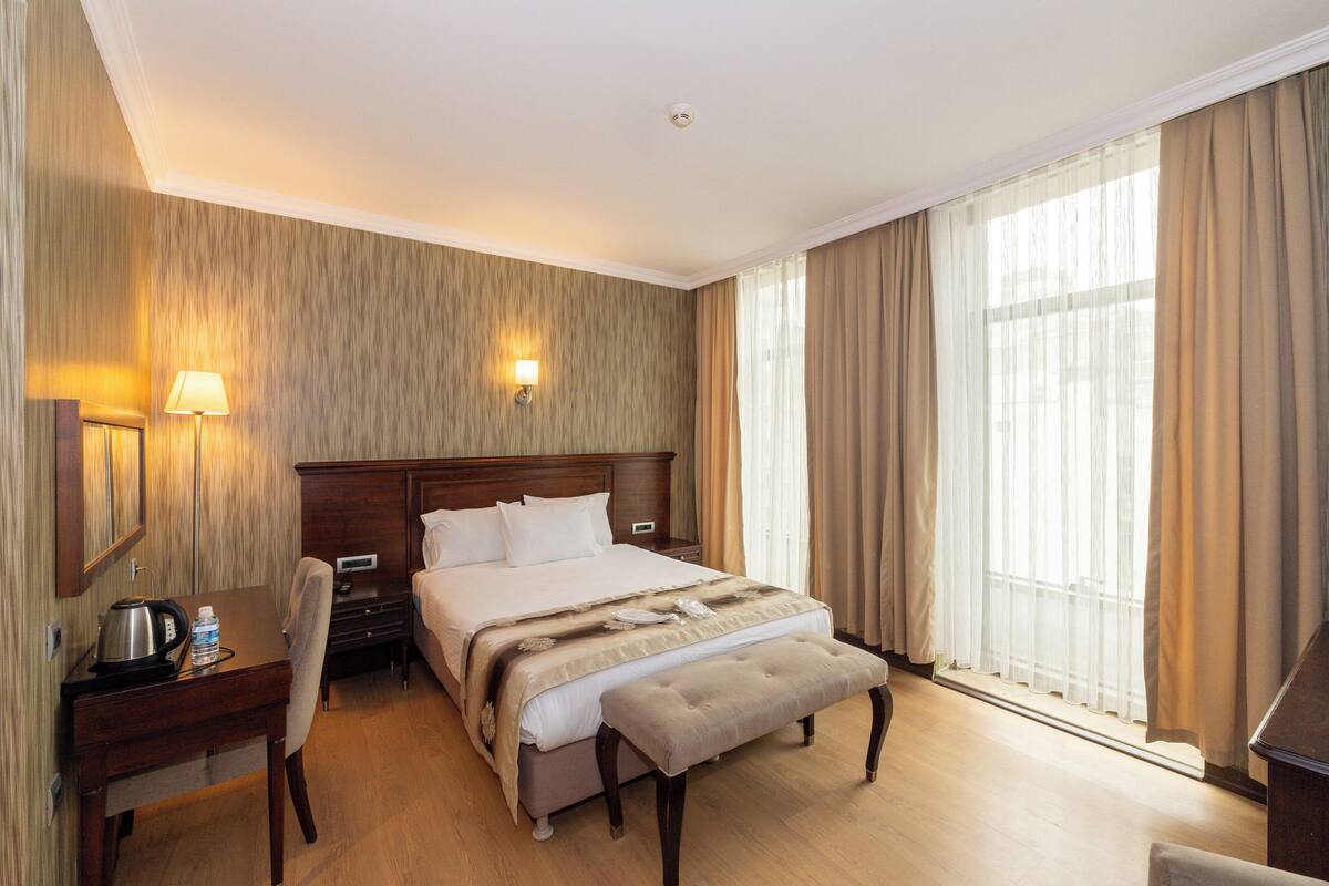 A hotel room with a bed, bedside table, lamp, and a desk with a chair.