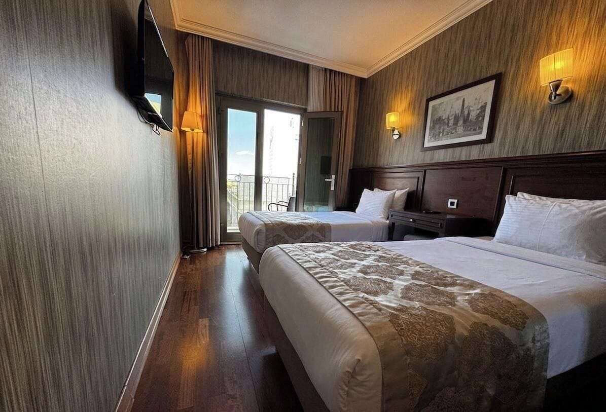 A hotel room with two beds, a television, a desk, and a balcony with a view.