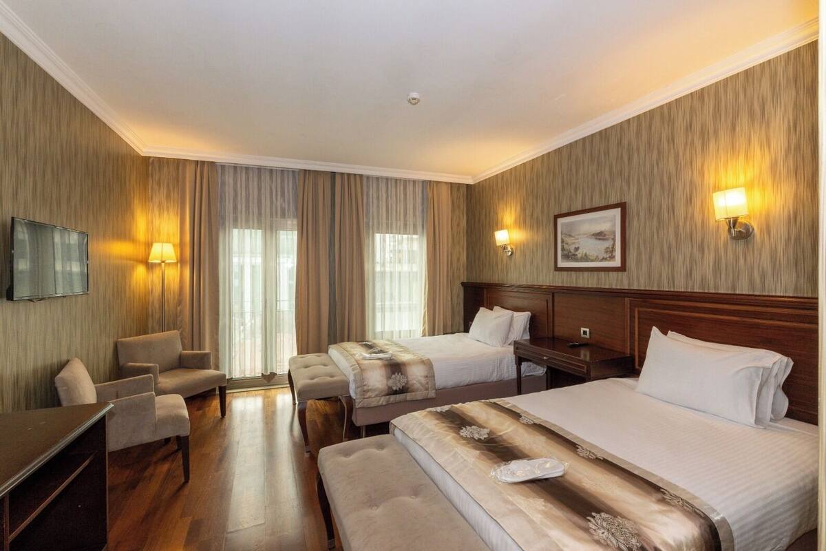 A hotel room with two beds, a desk, a chair, and a TV.