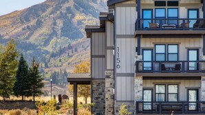 A multi-story building with a stone facade, numbered 1156, featuring balconies with outdoor seating and a view of a mountainous landscape.