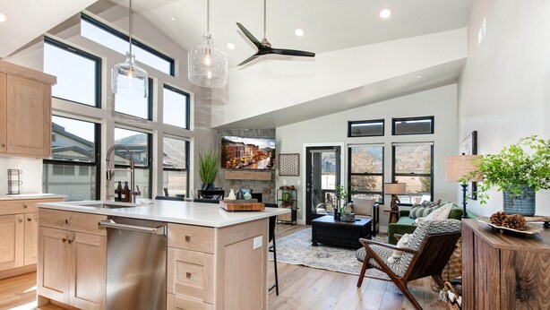 A spacious kitchen with a large island, wooden cabinets, and a view of the outdoors through large windows.