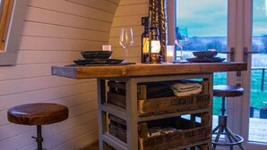 Un rústico área de bar con cajas de madera que dicen 'ASSOCIATED BRITISH' y 'BRITISH BRIEFS'. Hay dos taburetes y una copa de vino sobre la barra.