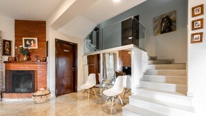 A modern living room with a fireplace, a staircase, and a dining area with white chairs. - Chalet Pinecone by Ezoria Villas (Platres)