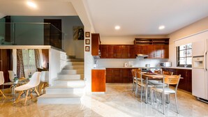 A modern kitchen with wooden cabinets, a dining area with a marble floor, and a staircase leading to an upper level. - Chalet Pinecone by Ezoria Villas (Platres)