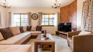 A living room with a sofa, armchairs, a coffee table, a TV, and a brick wall. - Chalet Pinecone by Ezoria Villas (Platres)