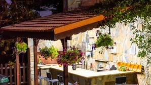 An outdoor patio with a stone wall, a wooden pergola, and a bar area with seating.