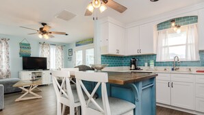 Une cuisine moderne avec des meubles blancs, un îlot central bleu et un ventilateur de plafond.