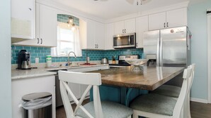 Une cuisine moderne avec des meubles blancs, un réfrigérateur en acier inoxydable, un four à micro-ondes et un îlot central en bois doté de chaises.