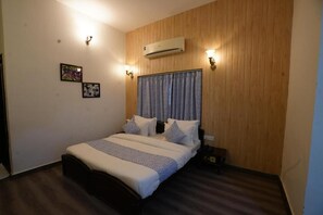 A bedroom with a wooden panel wall, a bed with patterned bedding, two wall-mounted lights, and an air conditioning unit. - Pansal Kothi - Best Boutique Hotel (Udaipur)