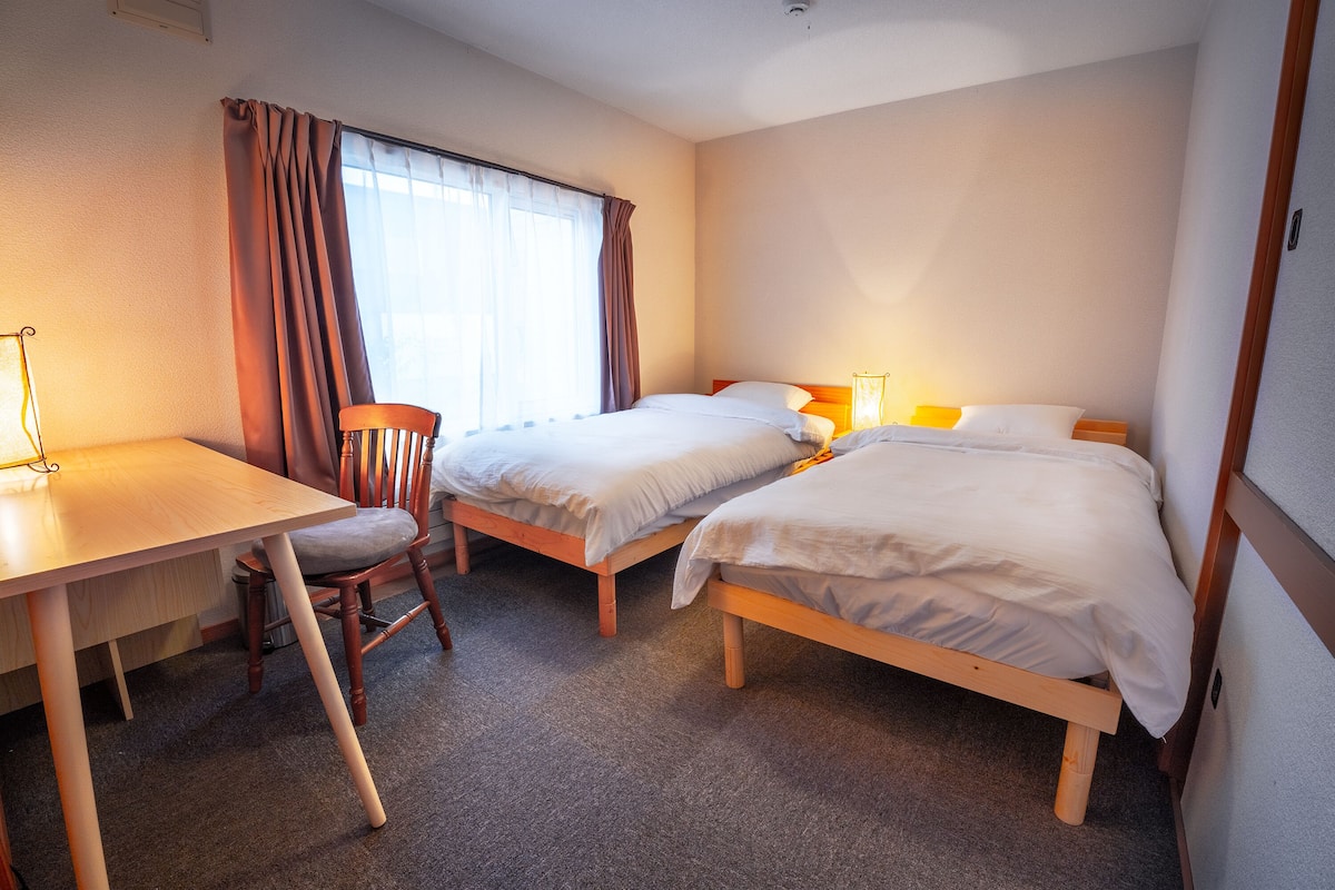 A hotel room with two single beds, a wooden desk, and a chair.