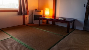 A room with tatami flooring, a low table with a book, a heater, and a window with curtains. - Winter Whale Lodge (Kutchan)