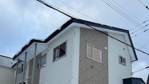 A two-story residential building with a covered front porch, a garage, and a staircase leading to the entrance. - Winter Whale Lodge (Kutchan)
