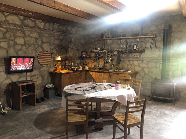 A rustic stone-walled room with a wooden table and chairs, a television, and a fireplace. - Elizbar Talakvadze Winery (Gurjaani)