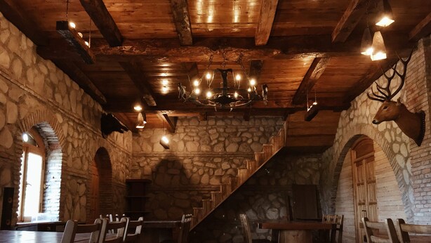 A rustic interior with stone walls, wooden beams, and a chandelier. Tables and chairs are arranged for dining. - Elizbar Talakvadze Winery (Gurjaani)