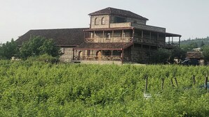 A two-story stone building with a balcony, surrounded by lush greenery. - Elizbar Talakvadze Winery (Gurjaani)