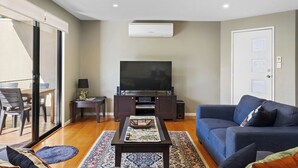 A living room with a flat-screen TV, dark wooden furniture, a blue sofa, and a patterned rug. - Tranquility on Thompson (Cowes)