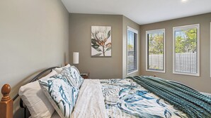 A bedroom with a bed, a nightstand, a lamp, and a window with blinds. - Tranquility on Thompson (Cowes)